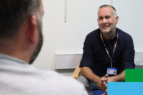 Staff member sits opposite another person smiling in a white room